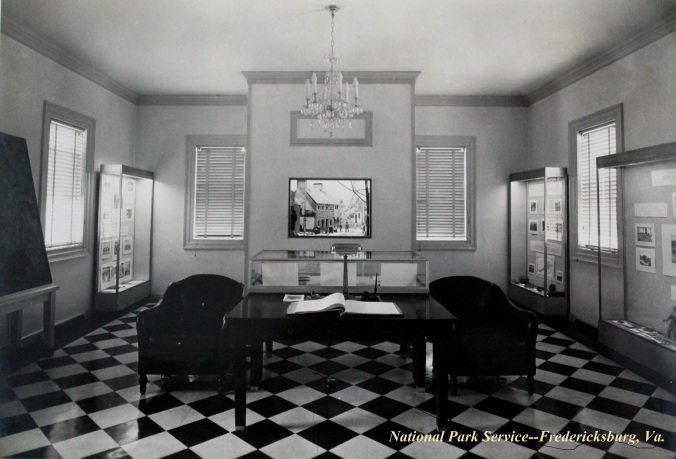 1937 view of Fredericksburg Battlefield museum and administrative building exhibits. Two chairs, a diorama of destruction downtown, four exhibit cases, and a large map.